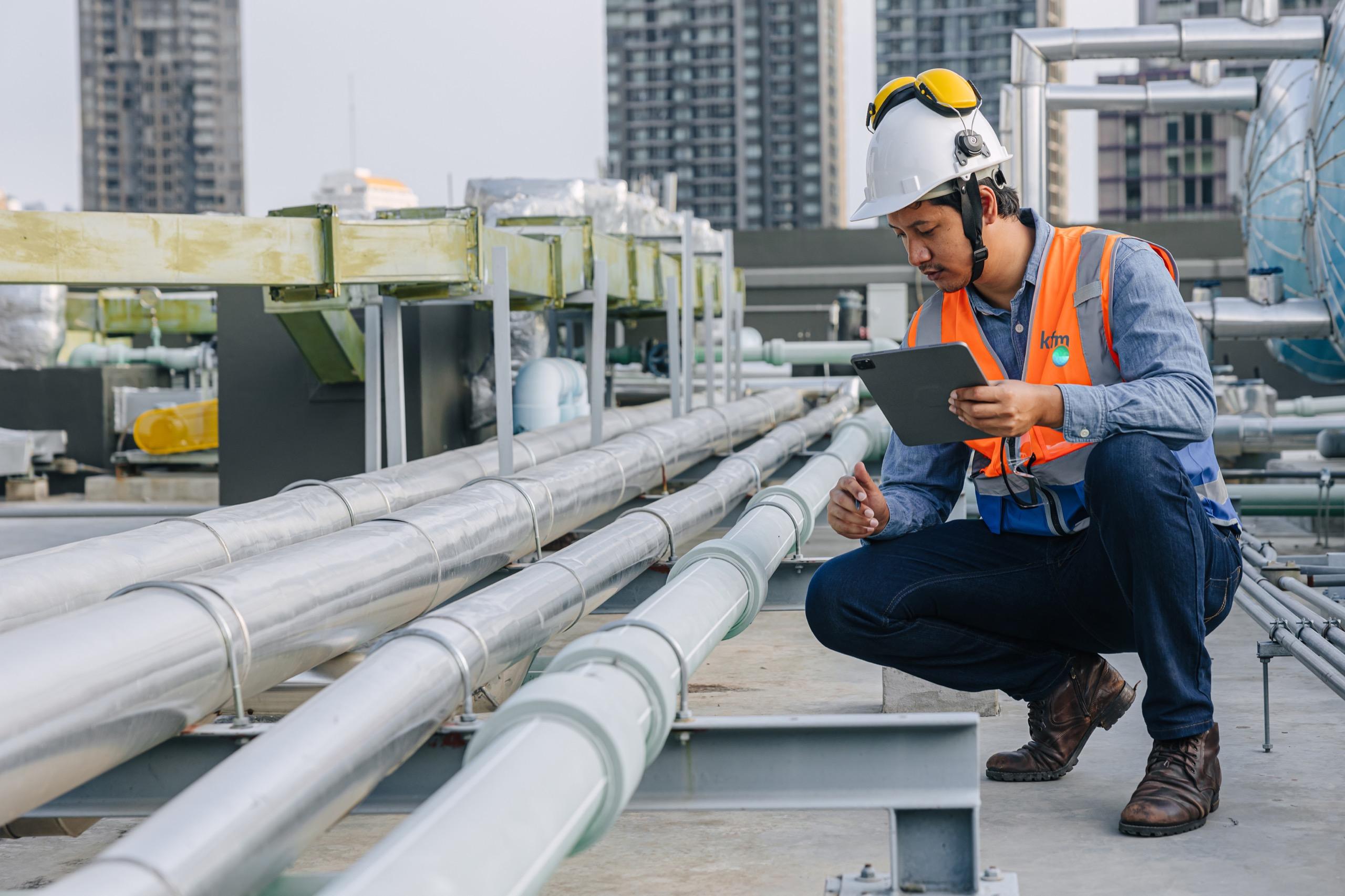 Engineer wearing safety helmet and vest checking industrial pipelines with a tablet.