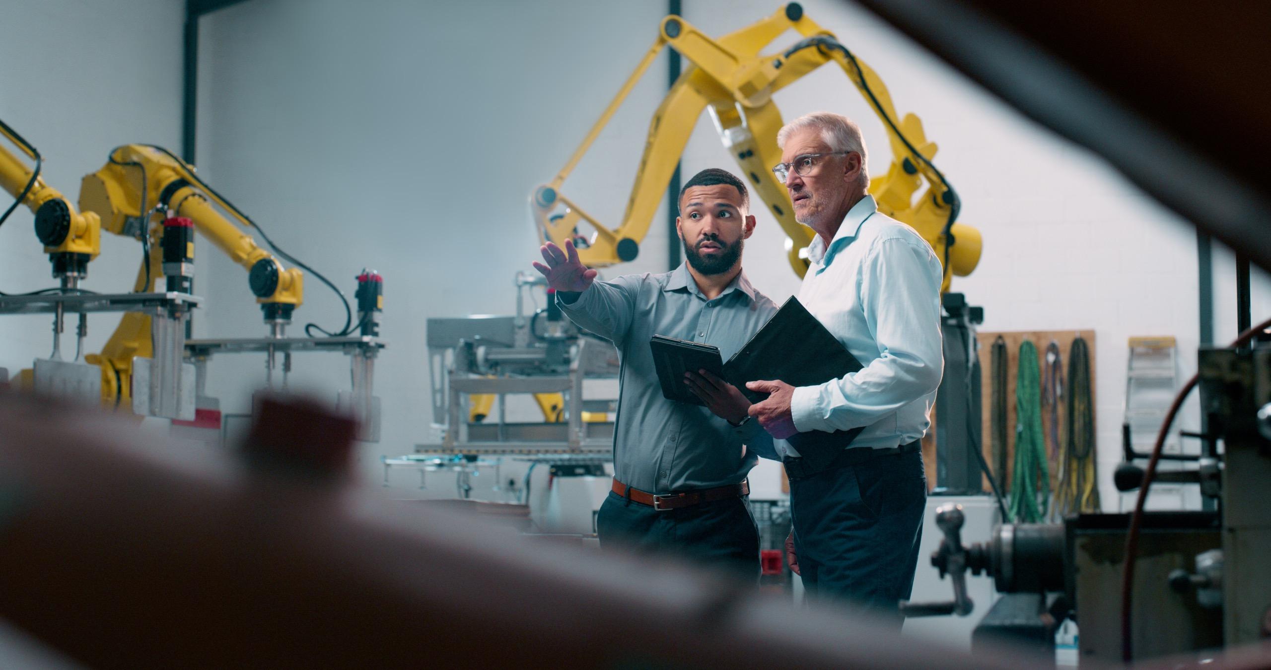 Engineers talking while standing beside industrial robotic machinery in a factory.