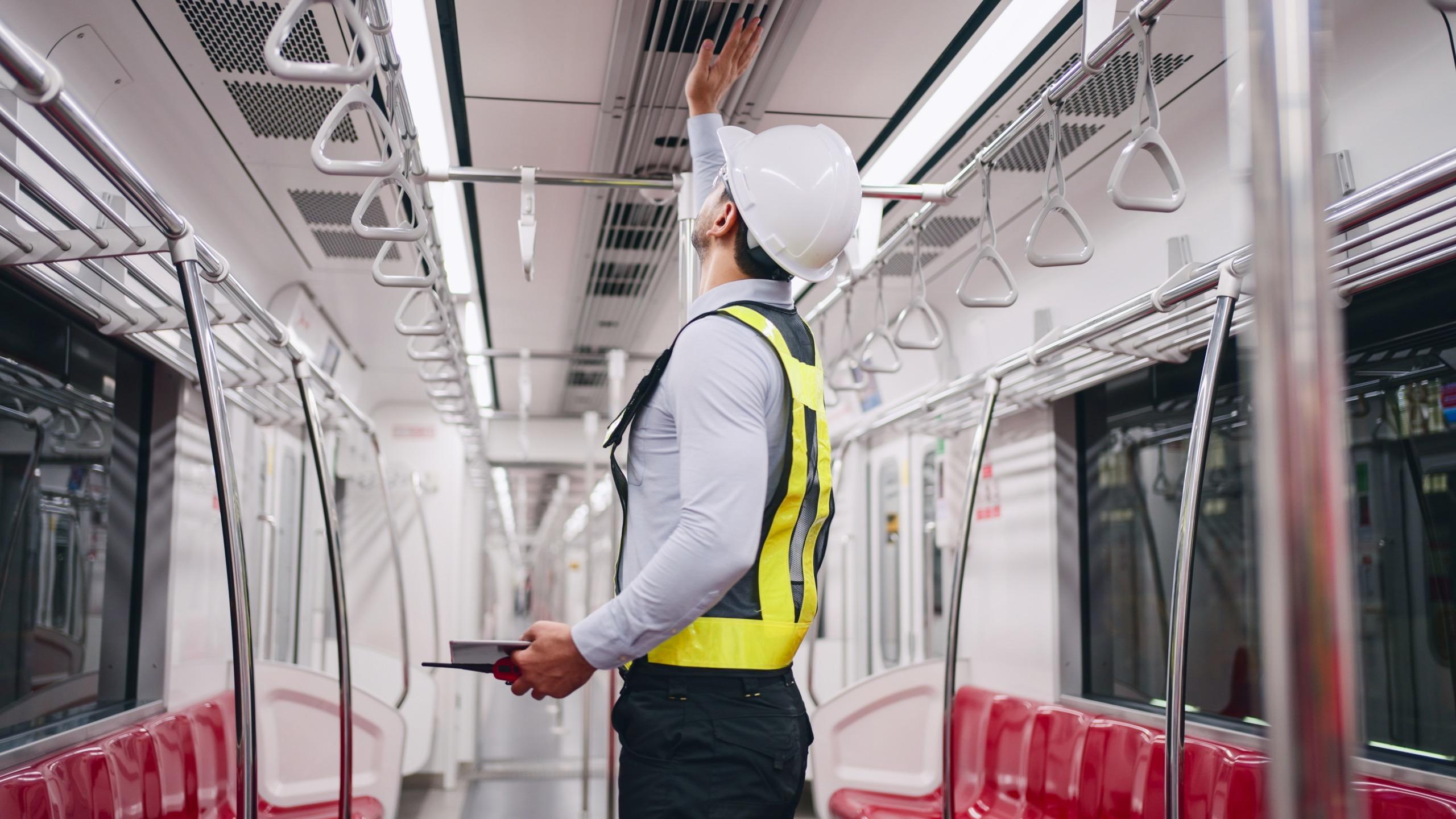 Engineer in hard hat inspecting carriage inside an empty metro train.