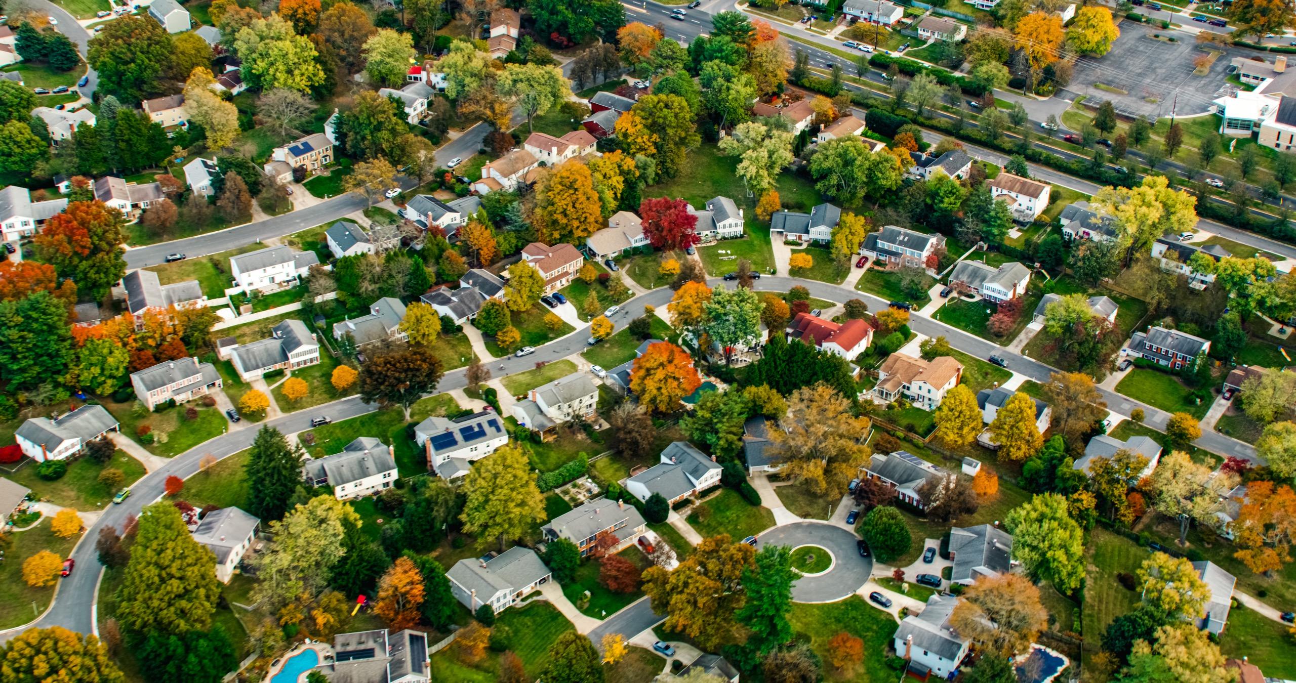 Aerial shot of a residential neighborhood with houses, roads, and colorful trees.