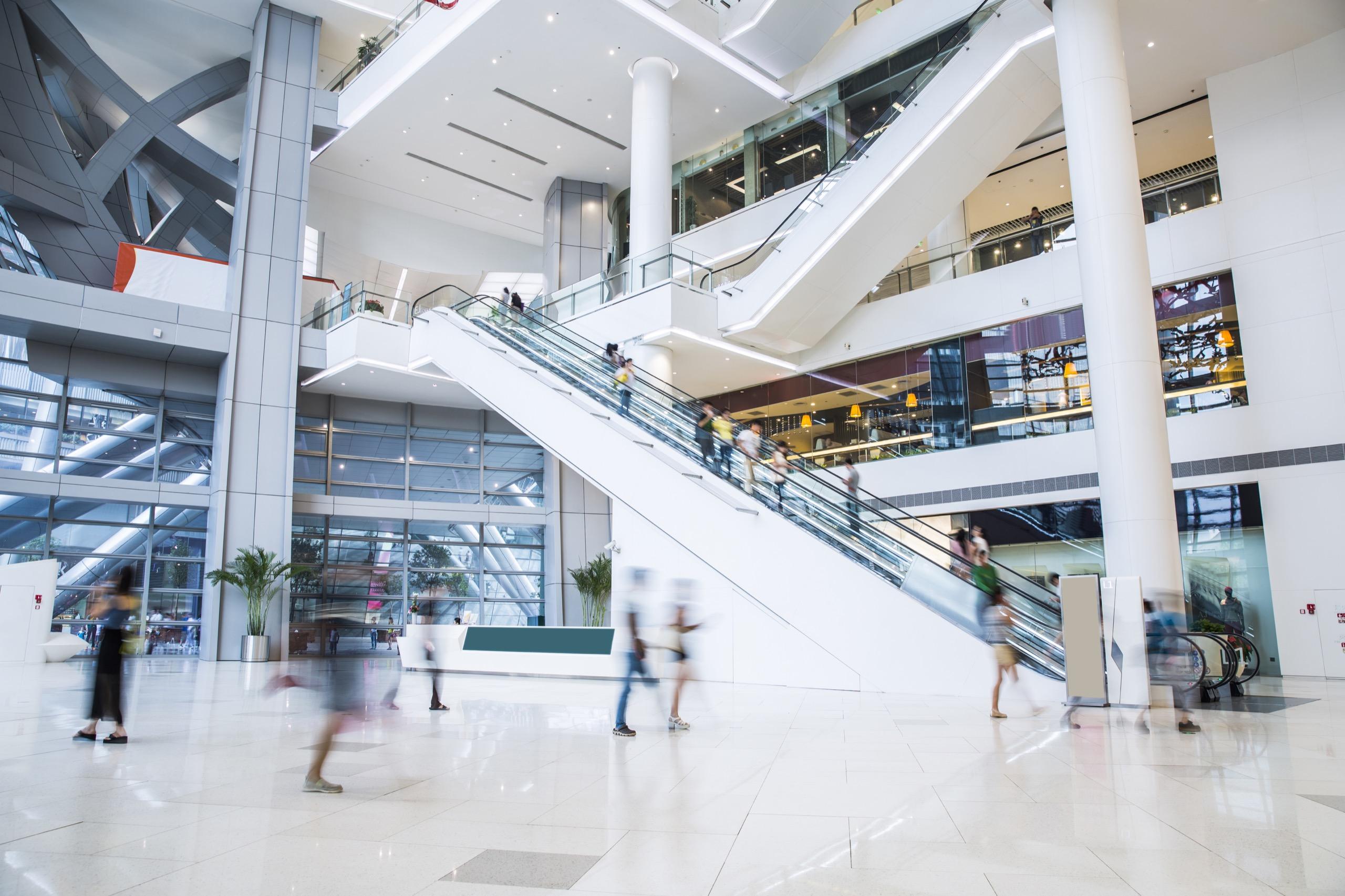 People using escalators inside a modern shopping mall with open glass design.