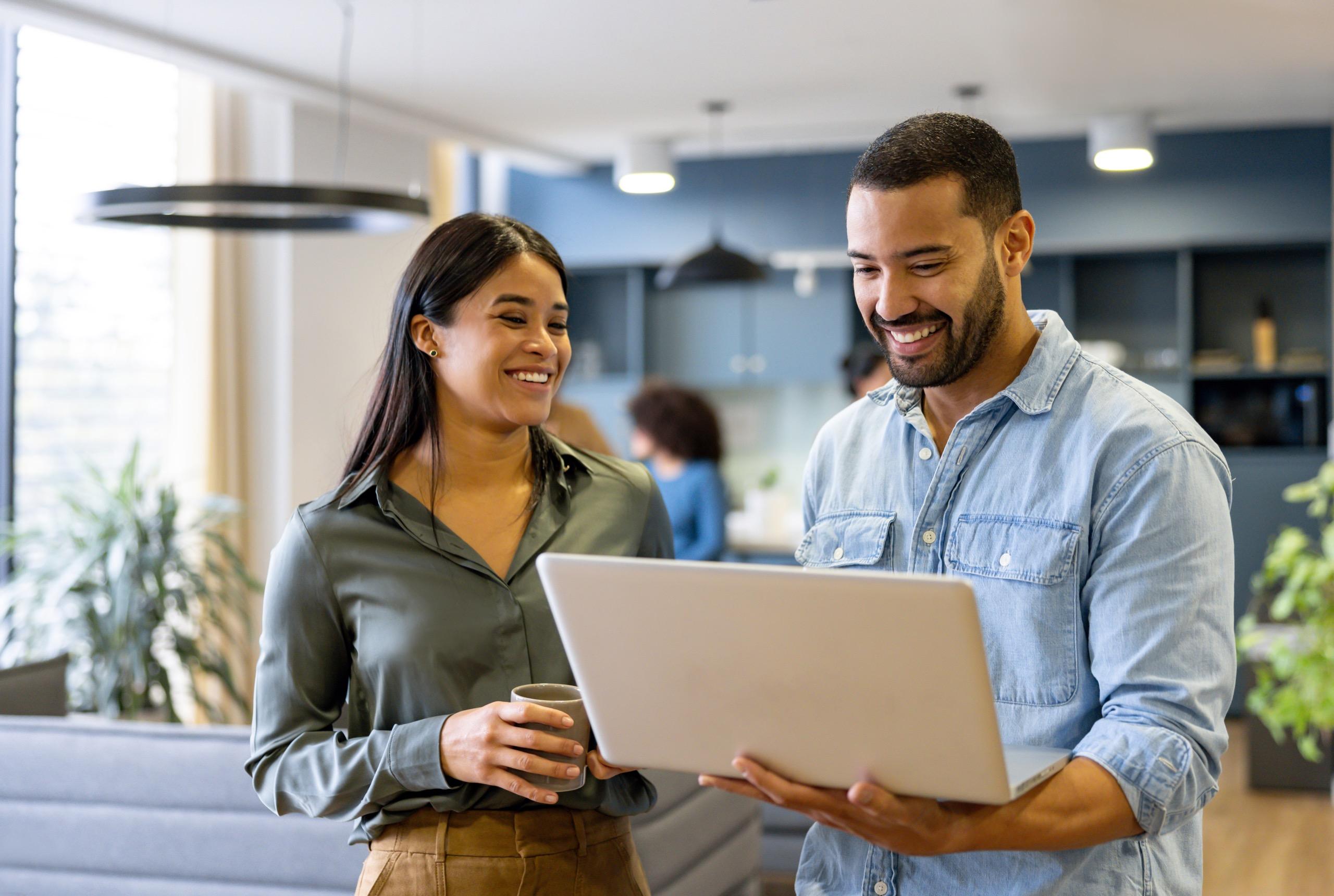 Smiling man and woman discussing work while looking at a laptop in an office.