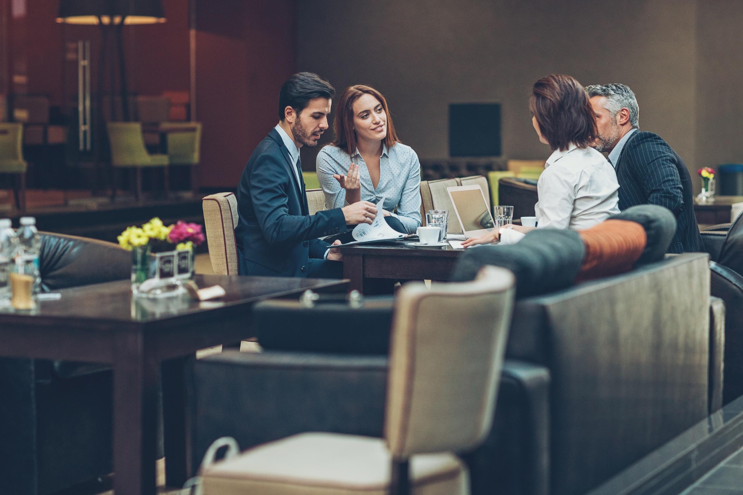 Group of business professionals sitting around a table discussing documents and ideas in a hospitality venue.
